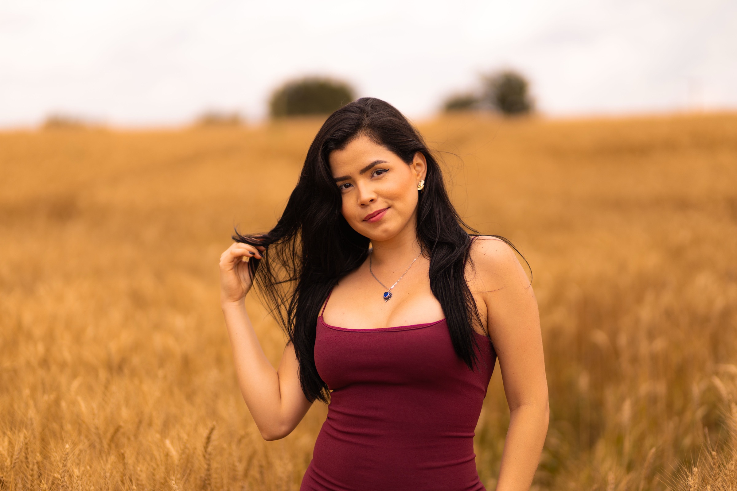 Retrato de una mujer con vestido guinda en un campo iluminado por luz naranja