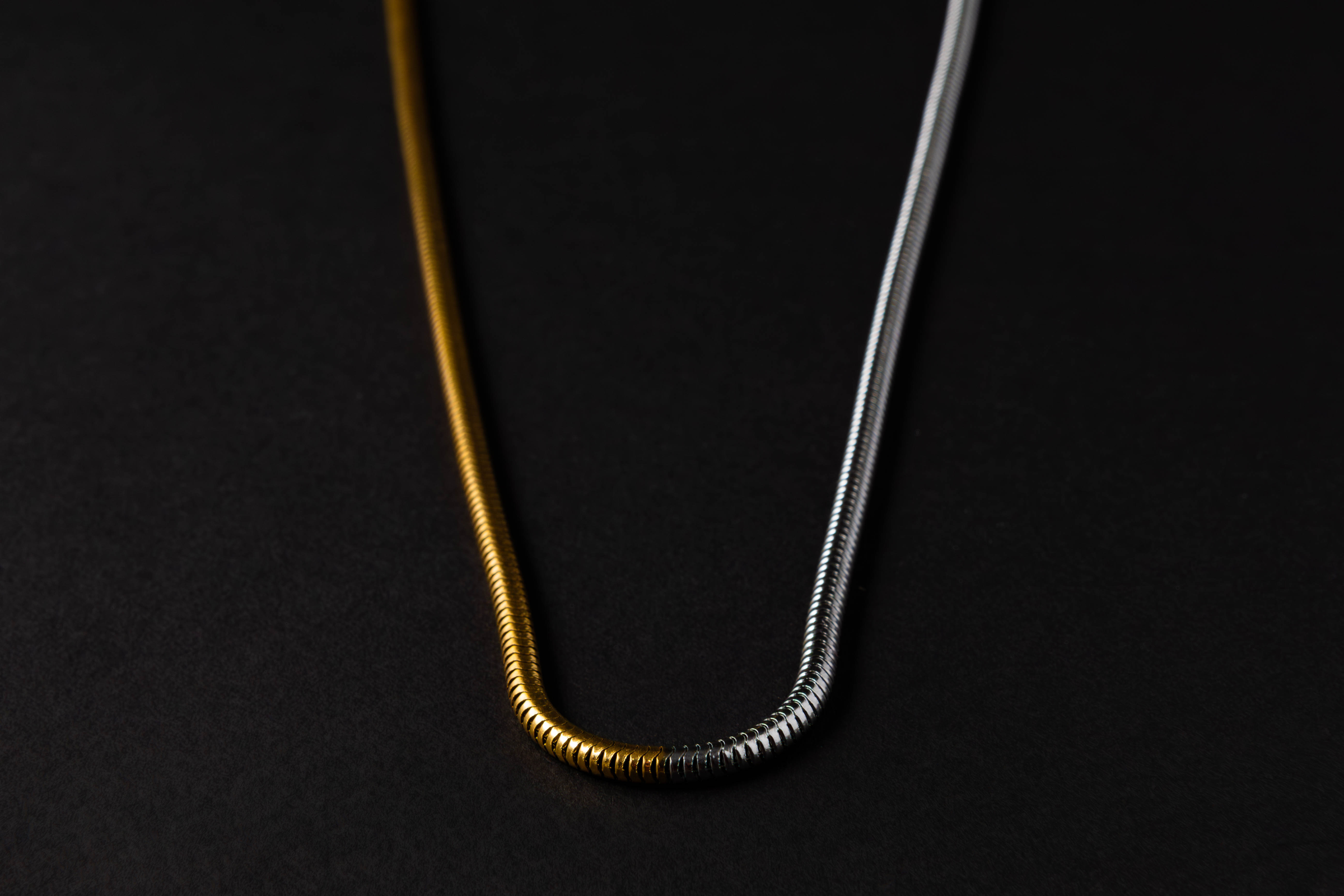 Fotografía de producto de un collar dorado y plateado sobre fondo negro