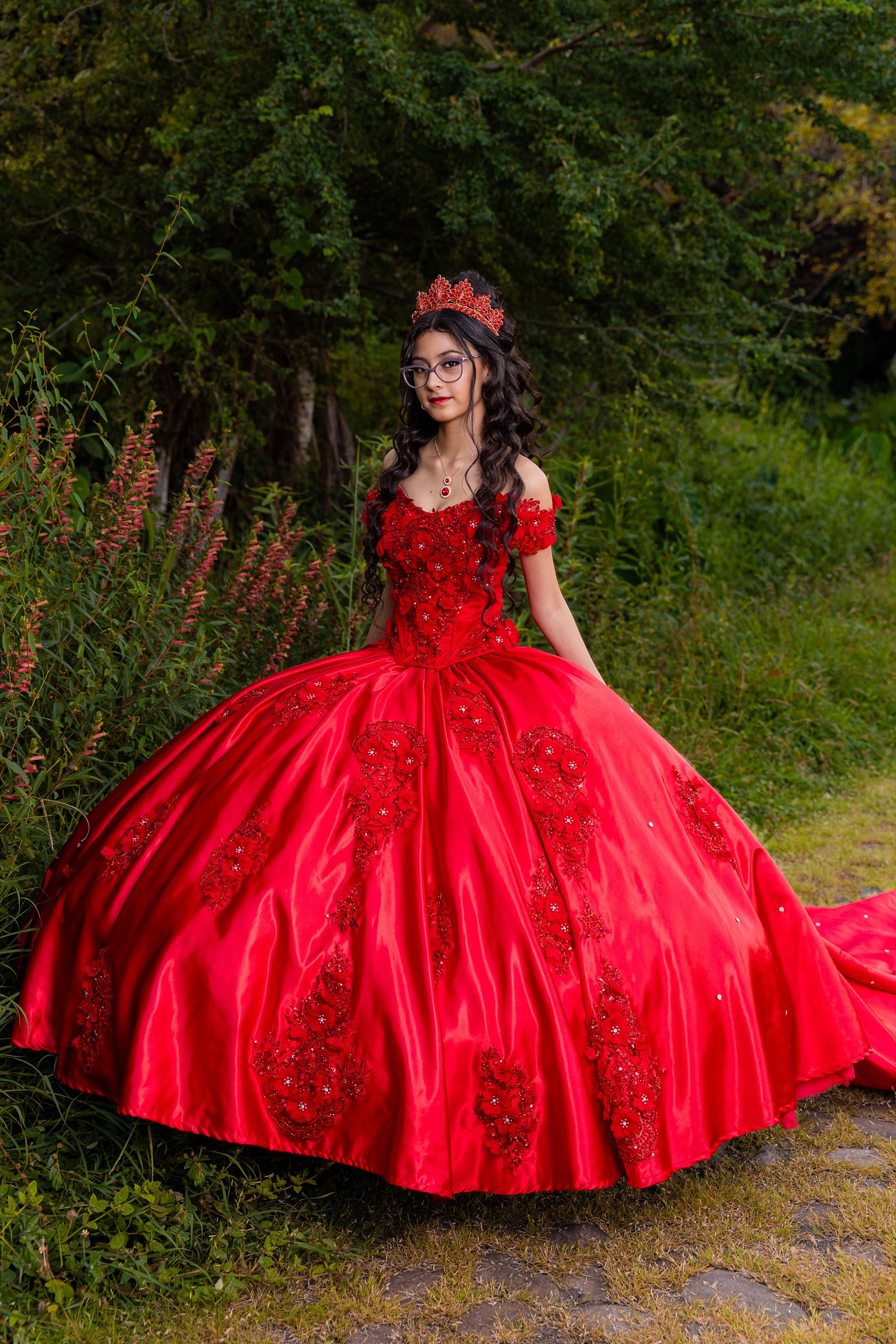 Retrato de una joven con vestido rojo y corona en un jardín